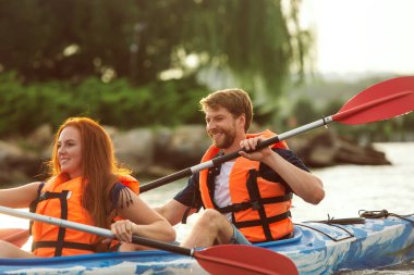 Mutlu çift nehirde kayak yapıyor, arka planda günbatımı var.