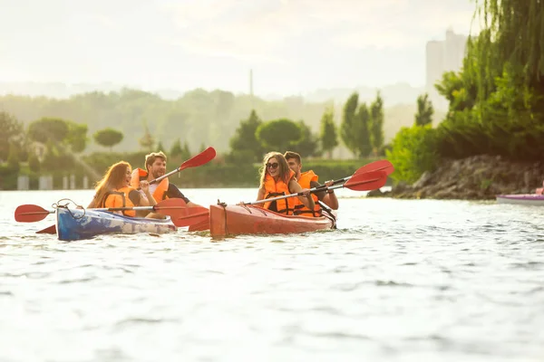 Heureux amis kayak sur la rivière avec coucher de soleil sur le fond — Photo