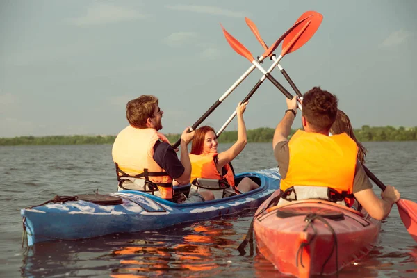 Lyckliga vänner kajakpaddling på floden med solnedgång på bakgrunden — Stockfoto