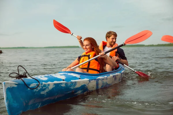 Glad par kajakpaddling på floden med solnedgång på bakgrunden — Stockfoto