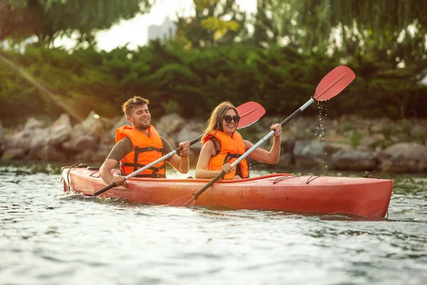 Glad par kajakpaddling på floden med solnedgång på bakgrunden — Stockfoto