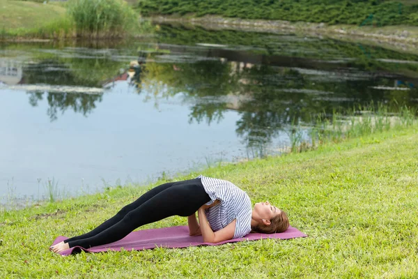 Jeune belle femme faisant de l'exercice de yoga dans un parc vert. Style de vie sain et concept de fitness . — Photo