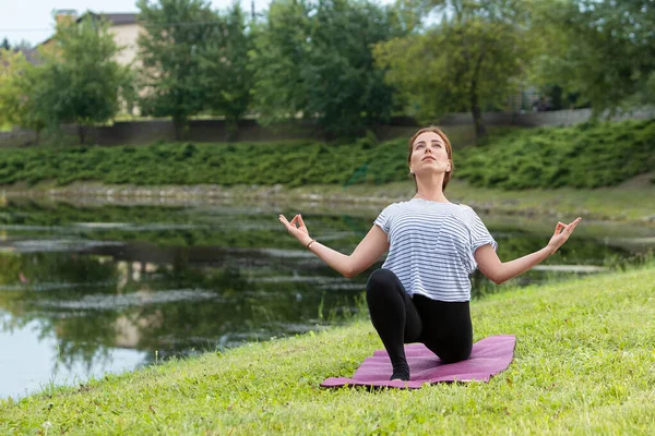 Jeune belle femme faisant de l'exercice de yoga dans un parc vert. Style de vie sain et concept de fitness . — Photo