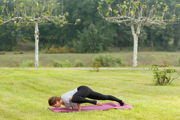 Jeune belle femme faisant de l'exercice de yoga dans un parc vert. Style de vie sain et concept de fitness . — Photo