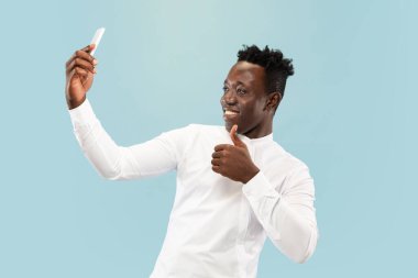 Genç Afro-Amerikalı adam mavi stüdyo arka planında izole edilmiş, insan duyguları konsepti..