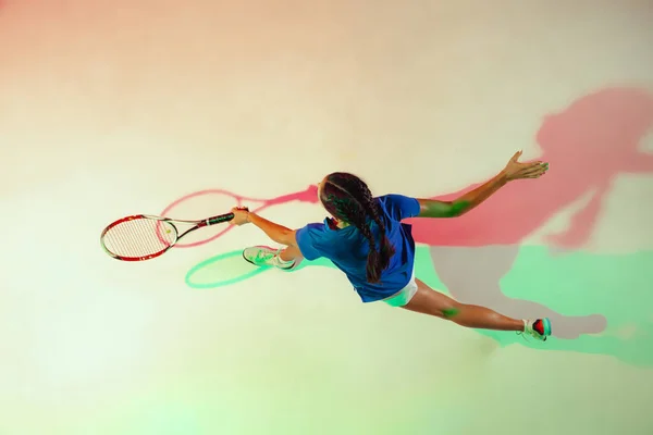 Ung kvinna i blå skjorta spelar tennis i blandat ljus. Ungdom, flexibilitet, kraft och energi. — Stockfoto