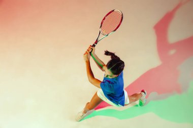 Mavi gömlekli genç bayan karışık ışıkta tenis oynuyor. Gençlik, esneklik, güç ve enerji.