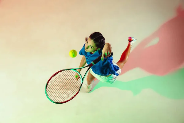 Ung kvinna i blå skjorta spelar tennis i blandat ljus. Ungdom, flexibilitet, kraft och energi. — Stockfoto