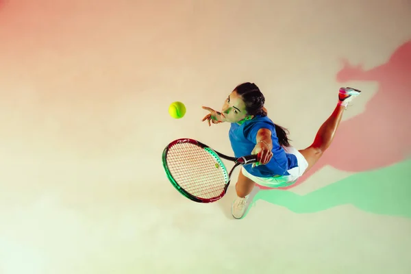 Ung kvinna i blå skjorta spelar tennis i blandat ljus. Ungdom, flexibilitet, kraft och energi. — Stockfoto