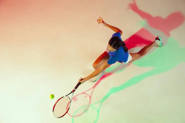 Mujer joven con camisa azul jugando al tenis con luz mixta. Juventud, flexibilidad, poder y energía . —  Fotos de Stock