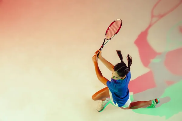 Ung kvinna i blå skjorta spelar tennis i blandat ljus. Ungdom, flexibilitet, kraft och energi. — Stockfoto