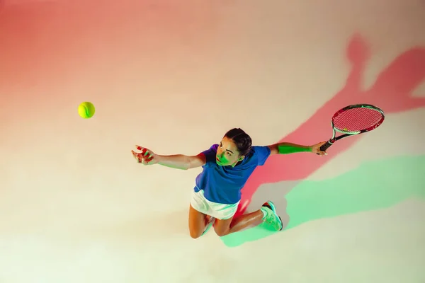 Young woman in blue shirt playing tennis in mixed light. Youth, flexibility, power and energy.