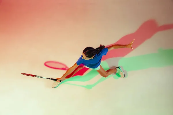 Ung kvinna i blå skjorta spelar tennis i blandat ljus. Ungdom, flexibilitet, kraft och energi. — Stockfoto