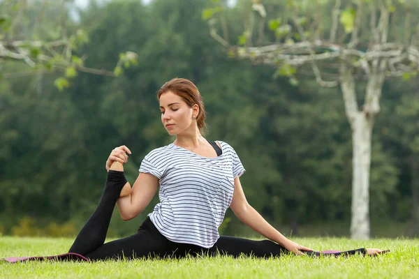 Ung vacker kvinna som motionerar yoga i grön park. Friska livsstil och fitness koncept. — Stockfoto