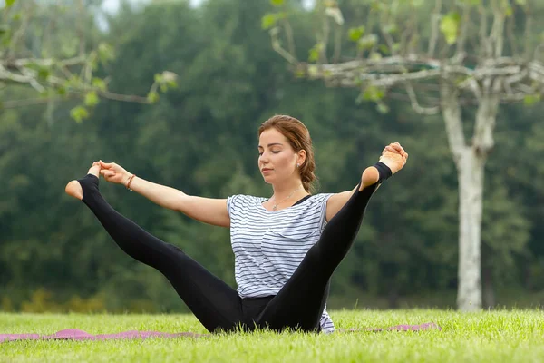 Jovem mulher bonita fazendo exercício de ioga no parque verde. Estilo de vida saudável e conceito de fitness . — Fotografia de Stock