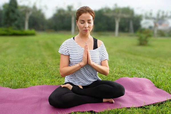 Jovem mulher bonita fazendo exercício de ioga no parque verde. Estilo de vida saudável e conceito de fitness . — Fotografia de Stock