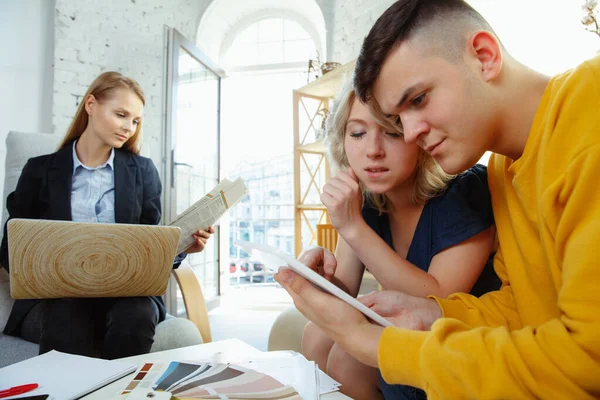 Diseñador de interiores trabajando con parejas jóvenes. Precioso diseñador familiar y profesional o arquitecto . — Foto de Stock