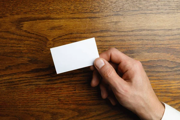 Mannelijke hand met een blanco visitekaartje op houten achtergrond voor tekst of ontwerp — Stockfoto