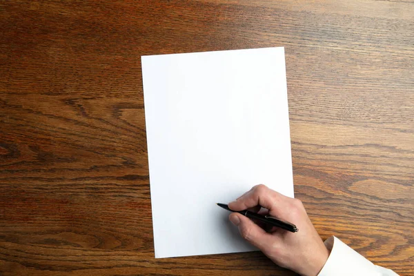 Male hand holding pen and writing on empty sheet on wooden background for text or design ストック写真