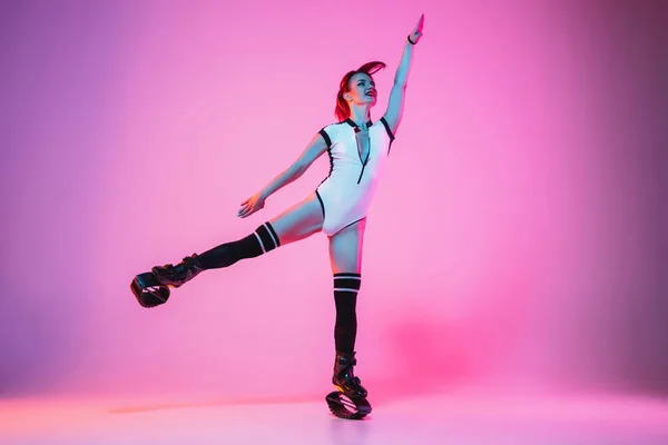 Mulher ruiva bonita em um sportswear branco pulando em um kangoo salta sapatos isolados no fundo do estúdio gradiente em luz de néon — Fotografia de Stock