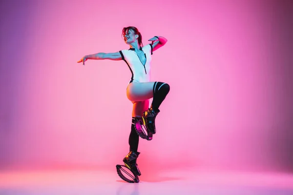 Belle femme rousse en tenue de sport blanche sautant dans un kangoo saute des chaussures isolées sur fond de studio dégradé au néon — Photo
