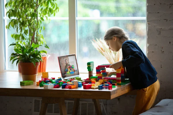 Dívka si hraje s konstruktérem doma, dívá se na výuku učitelů na notebooku. Digitalizace, vzdálené vzdělávání — Stock fotografie