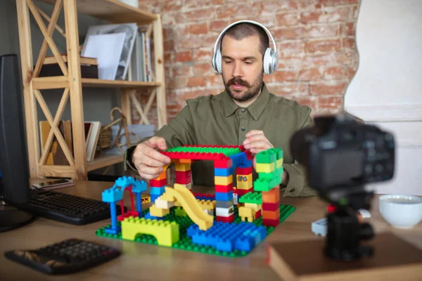 Man giving online lesson with constructor at home. Recording teachers tutorial on camera for kids. Digitalization, remote education