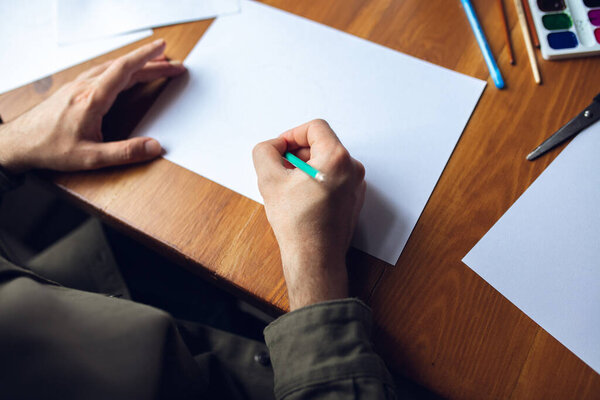 Крупным планом человек рисует красками и карандашами дома. Дистанционное образование, творческая профессия, арт-терапия
