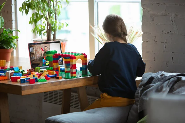 Girl playing with constructor at home, watching teachers tutorial on laptop. Digitalization, remote education — Stock Photo, Image