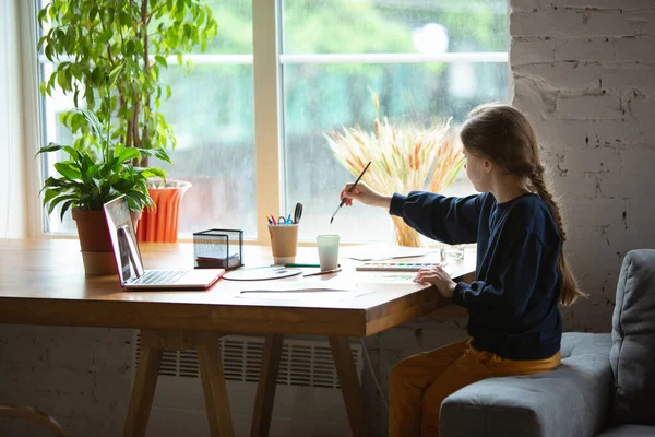 Ragazza che disegna con vernici e matite a casa, guardando insegnanti tutorial sul computer portatile. Digitalizzazione, istruzione a distanza — Foto Stock