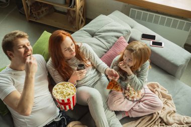 Aile evde birlikte güzel vakit geçiriyor, mutlu ve neşeli görünüyor, televizyon seyrediyor.