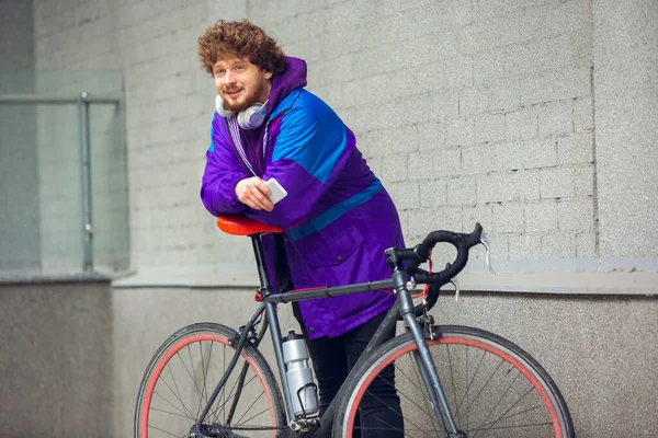 Beau jeune homme utilisant téléphone portable et écouteurs tout en se tenant près de son vélo à côté de lui — Photo