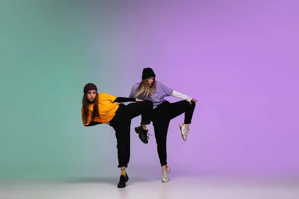 Girls dancing hip-hop in stylish clothes on gradient background at dance hall in neon light. — Stock Photo, Image