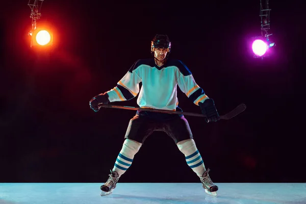 Jugador de hockey masculino con el palo en la pista de hielo y fondo de color neón oscuro — Foto de Stock