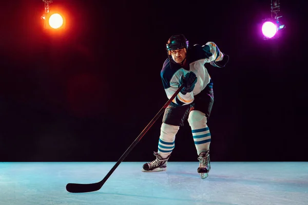 Jugador de hockey masculino con el palo en la pista de hielo y fondo de color neón oscuro — Foto de Stock