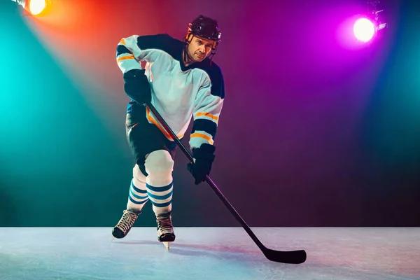 Jogador de hóquei masculino com a vara na quadra de gelo e neon escuro colorido fundo — Fotografia de Stock
