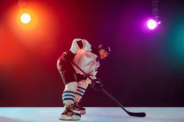 Jugador de hockey masculino con el palo en la pista de hielo y fondo de color neón oscuro — Foto de Stock