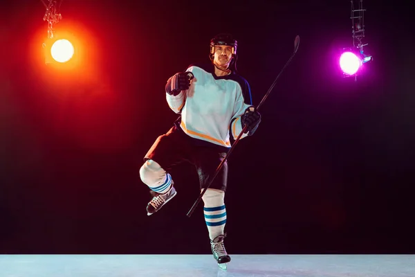 Jugador de hockey masculino con el palo en la pista de hielo y fondo de color neón oscuro — Foto de Stock