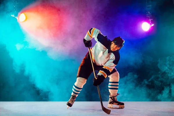 Jugador de hockey masculino con el palo en la pista de hielo y fondo de color neón oscuro — Foto de Stock