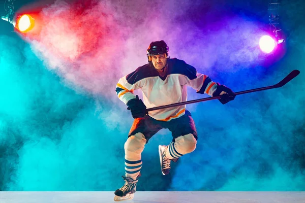 Jugador de hockey masculino con el palo en la pista de hielo y fondo de color neón oscuro — Foto de Stock