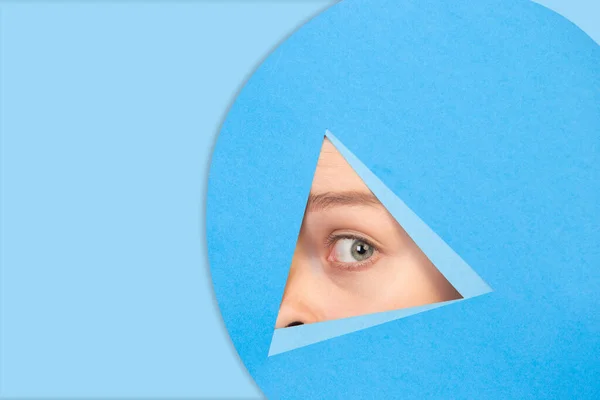 Mujer mirando a los ojos, mirando a través del triángulo en el fondo azul — Foto de Stock