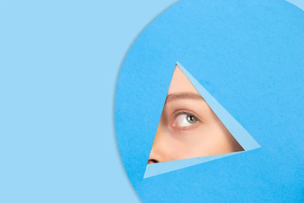 Female eye looking, peeking throught triangle in blue background