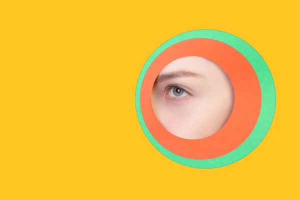 Olho feminino espreitando através do círculo em fundo amarelo — Fotografia de Stock