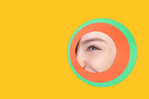 Ojo femenino que mira a través del círculo en el fondo amarillo — Foto de Stock