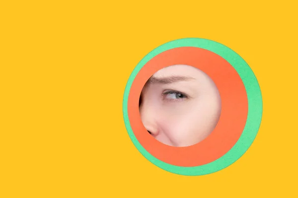 Occhio femminile sbirciando cerchio attraverso lo sfondo giallo — Foto Stock