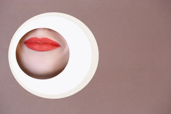 Cara femenina con labios rojos asomándose a través del círculo en fondo marrón — Foto de Stock