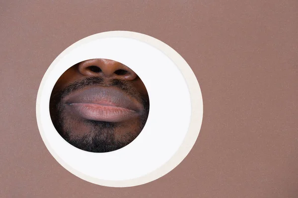 Labios de hombre afroamericano mirando a través del círculo en un fondo marrón — Foto de Stock