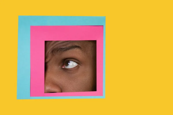 Olho de homem afro-americano espreitando através da praça em fundo amarelo — Fotografia de Stock