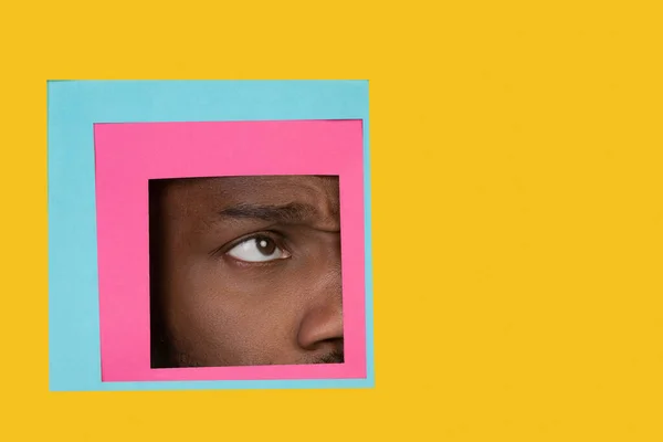 Auge eines afrikanisch-amerikanischen Mannes, der durch ein Quadrat in gelbem Hintergrund blickt — Stockfoto