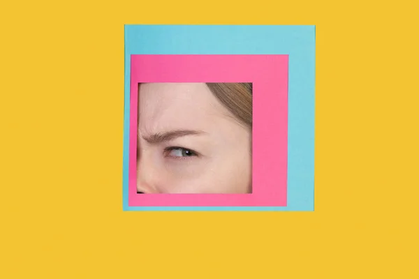 Rosto de mulher caucasiana espreitando através de quadrado em fundo amarelo — Fotografia de Stock